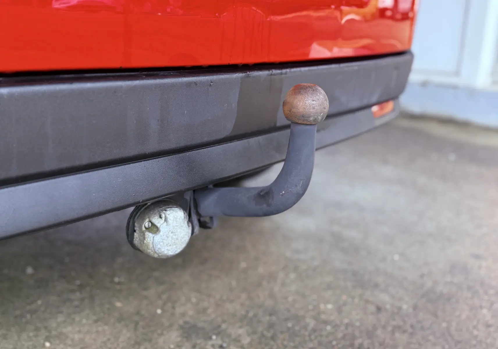 Gros plan sur l'attelage d'une FIAT Doblo Cargo rouge, avec pare-chocs arrière noir visible en arrière-plan.