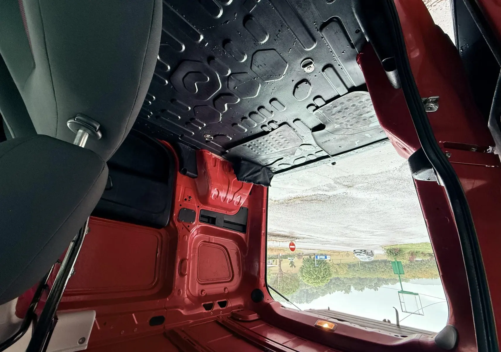Vue intérieure arrière du Fiat Doblo Cargo rouge, montrant l’espace de chargement vide et la porte ouverte côté droit.