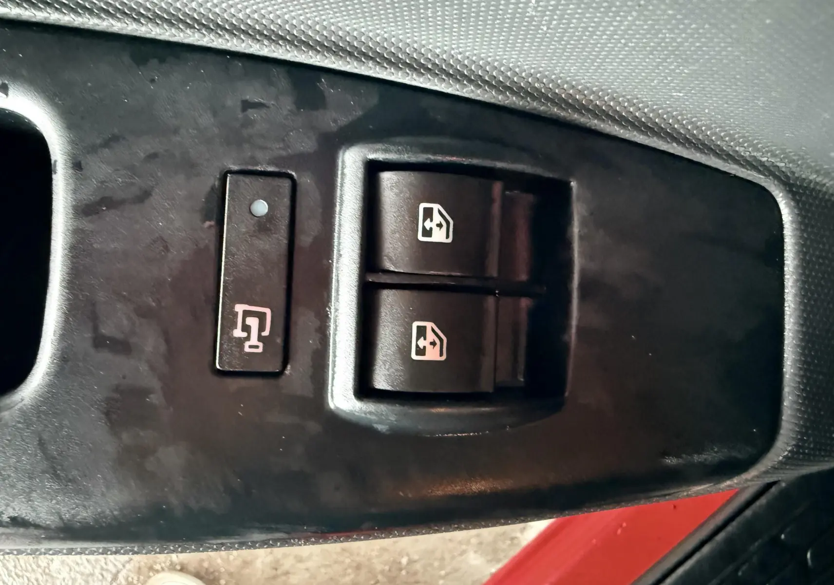 Gros plan sur les commandes des vitres électriques côté conducteur du Fiat Doblo Cargo rouge, avec bouton de verrouillage.