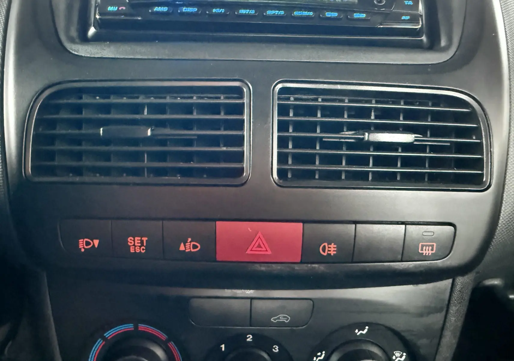 Vue rapprochée du tableau de bord noir du Fiat Doblo Cargo 2011, montrant les aérateurs centraux et les commandes de climatisation.