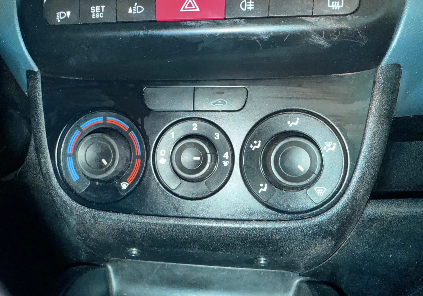 Vue rapprochée des commandes de climatisation et des boutons de sécurité du tableau de bord du Fiat Doblo Cargo 2011.