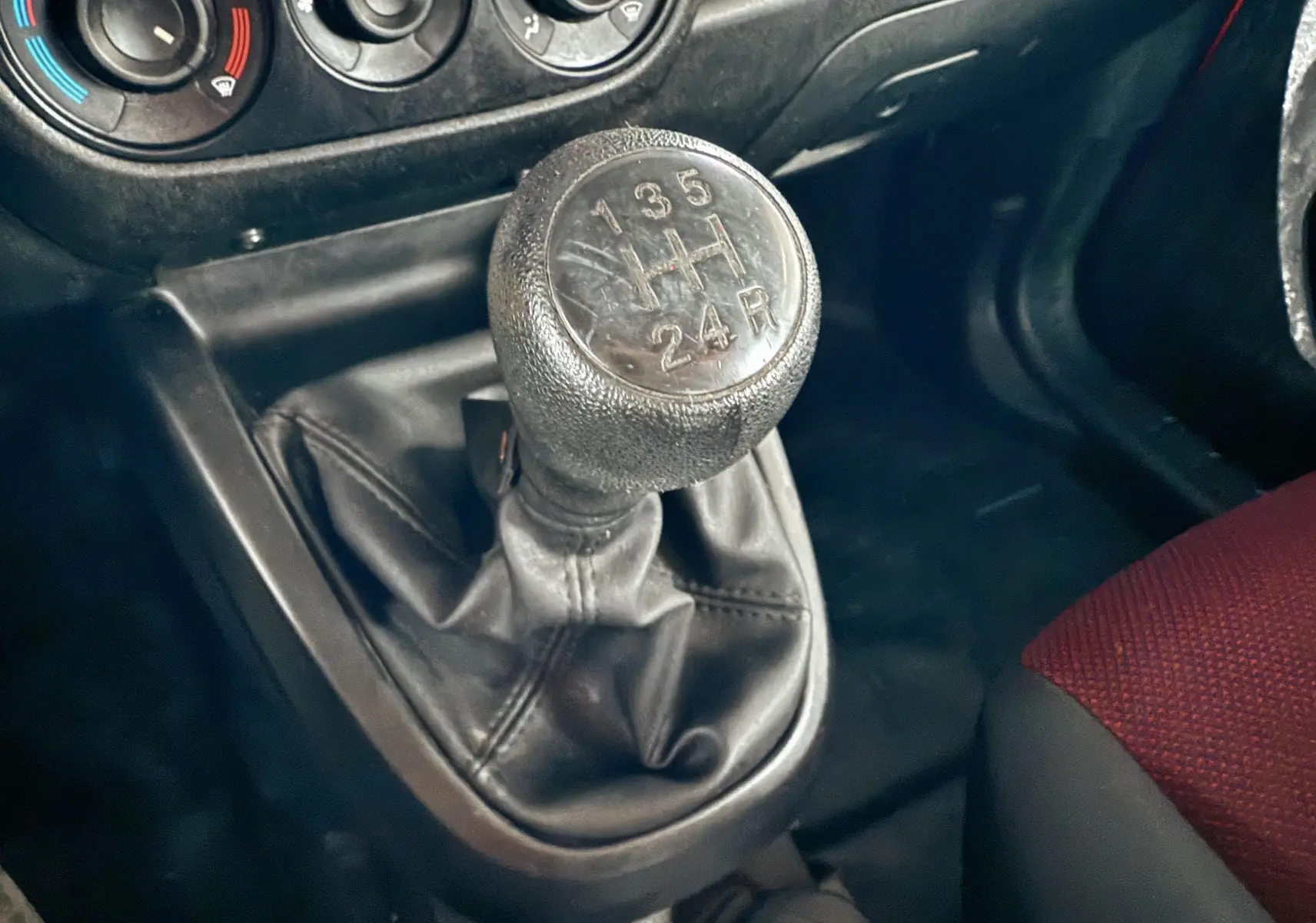 Gros plan sur le levier de vitesses manuel noir du Fiat Doblo Cargo 2011 avec siège tissu rouge visible à droite.