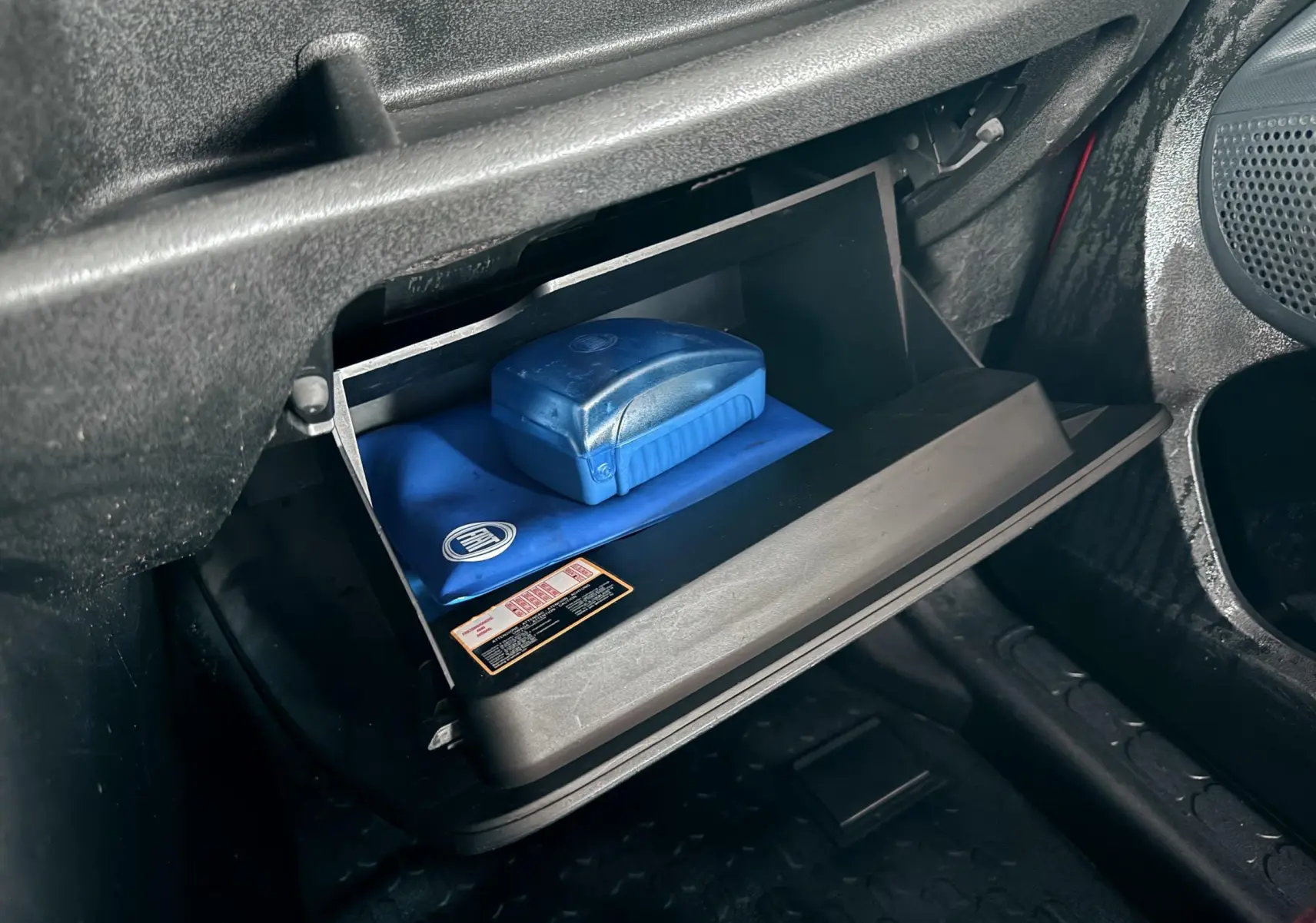Vue rapprochée de la boîte à gants ouverte du Fiat Doblo Cargo 2011, contenant une trousse bleue avec logo Fiat.