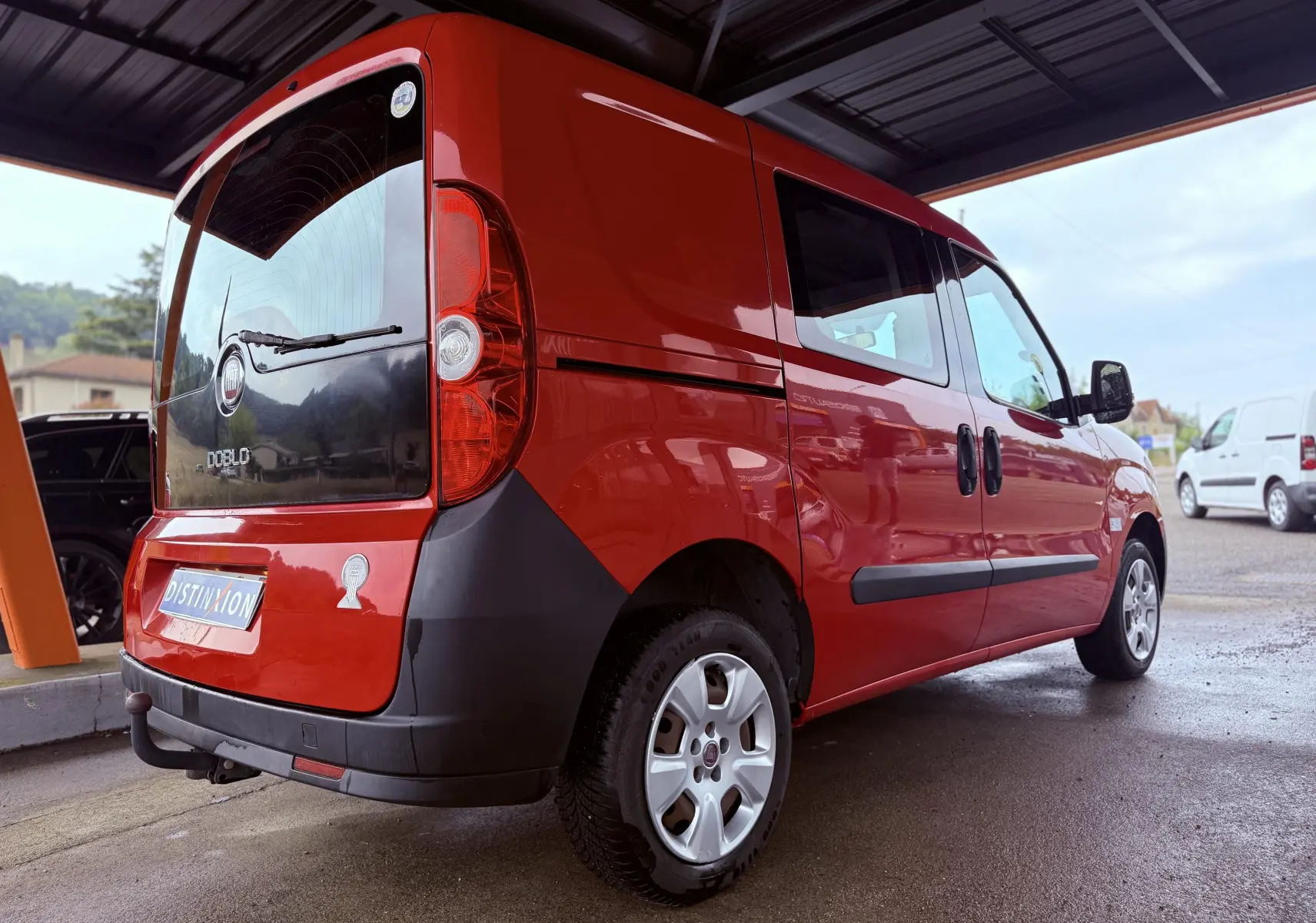 Fiat Doblo Cargo rouge vu en 3/4 arrière droit sous abri, avec hayon arrière noir et jantes argentées.