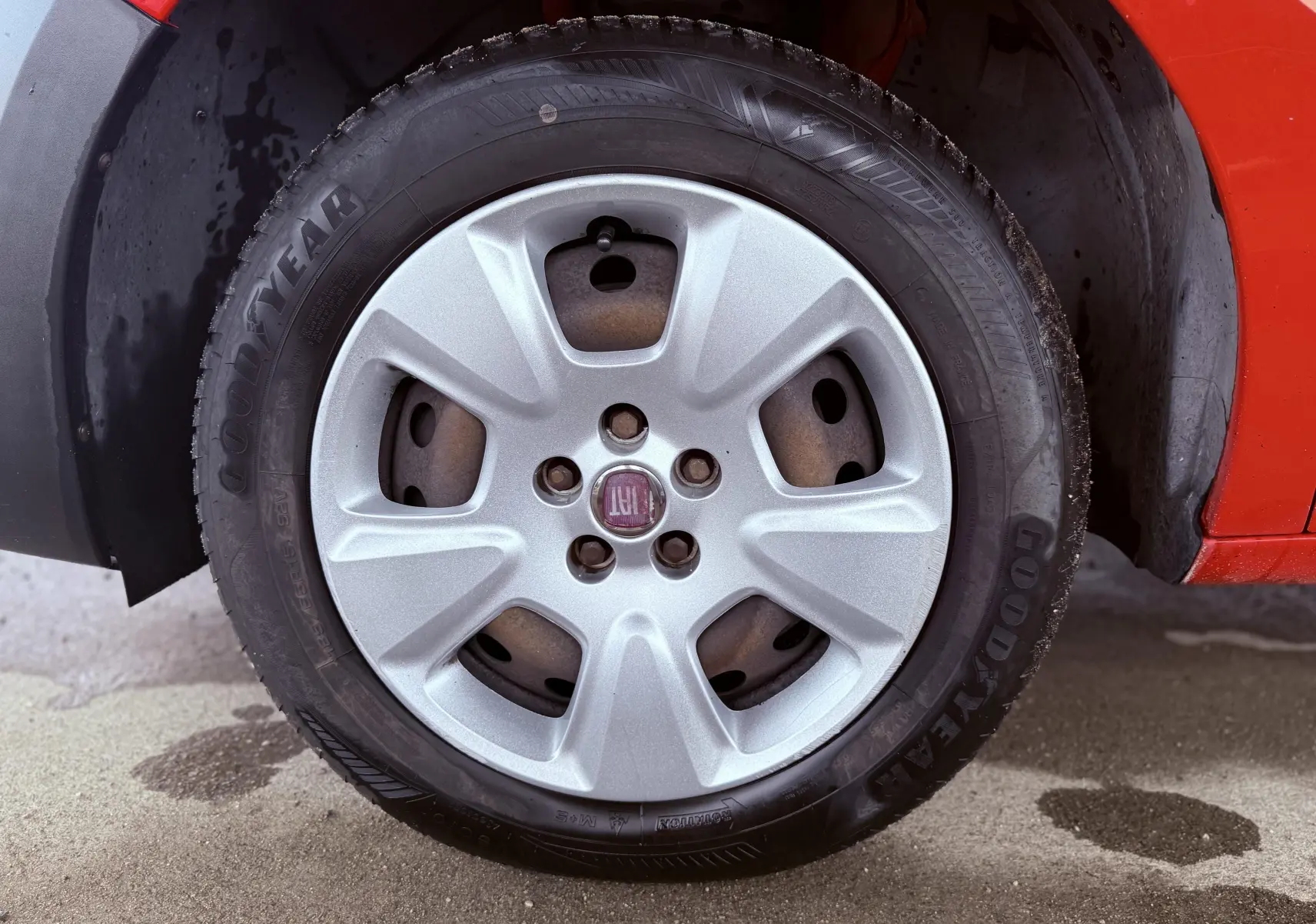 Gros plan sur la roue avant gauche d’un FIAT Doblo Cargo rouge de 2011 avec jante argentée et pneu Goodyear.