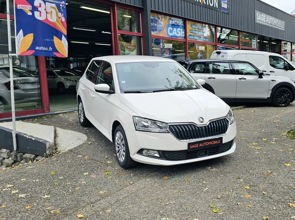 SKODA Fabia blanc cristal vue 3/4 avant garée devant un garage avec enseigne Sage Automobile.