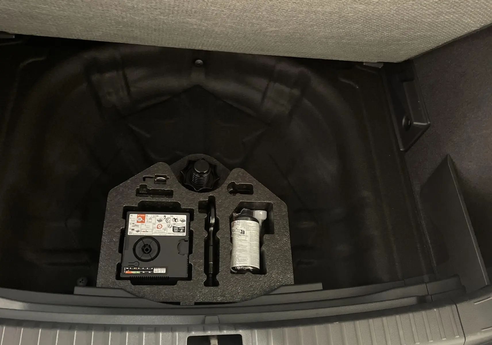 Coffre ouvert du SEAT Ateca blanc Nevada 2024, vue sur le rangement sous plancher avec kit de réparation pneus.