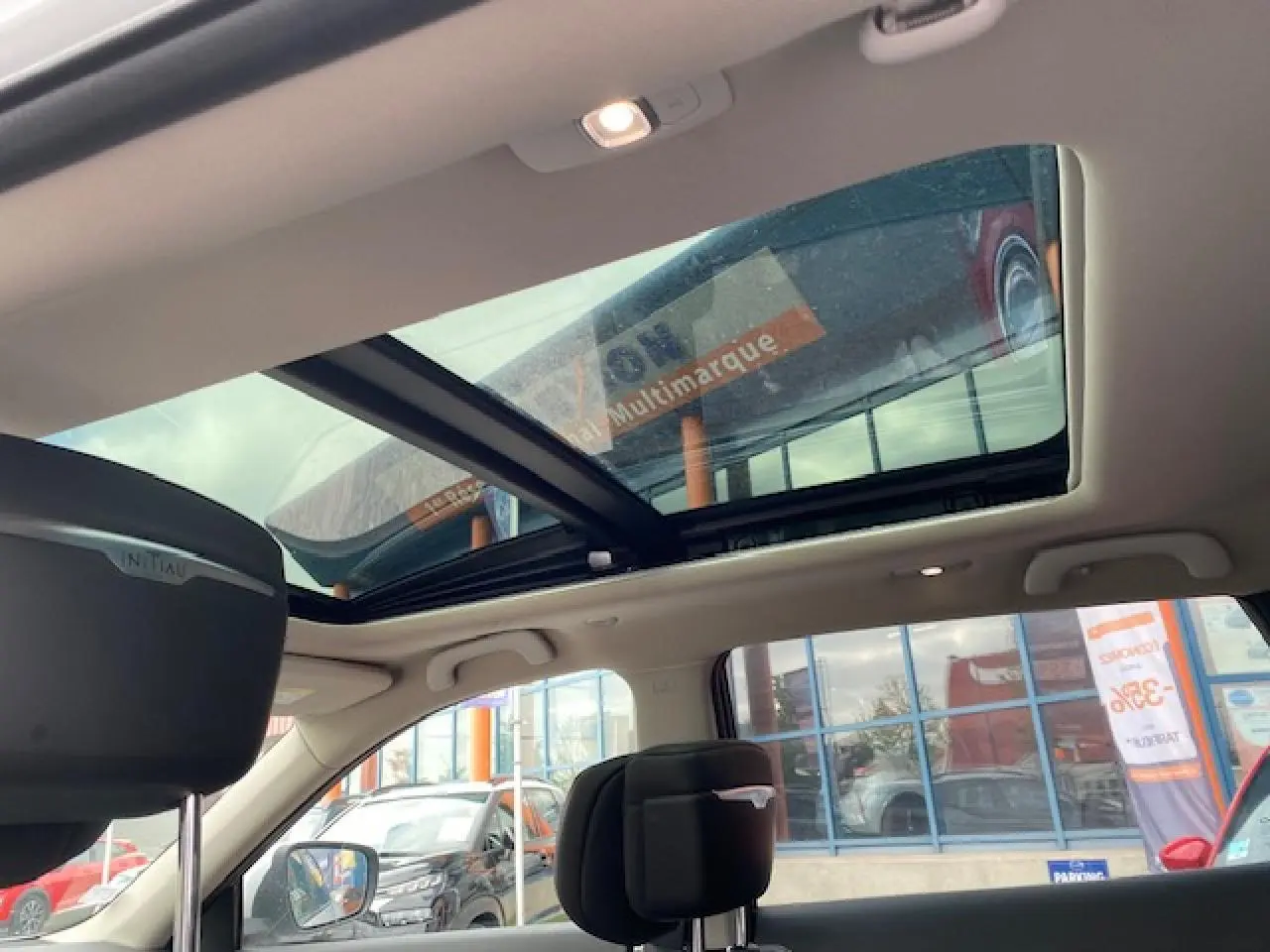 Toit panoramique ouvert sur l'intérieur d'un Renault Koleos blanc 2019, vue côté gauche avec appuie-tête Initiale Paris.