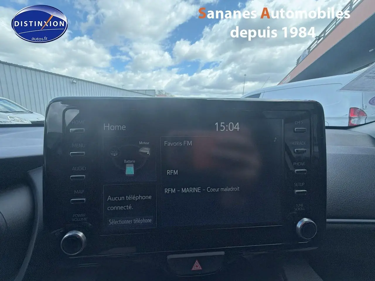 Écran tactile central de la Toyota Yaris Hybrid 2023, affichant la radio FM, avec tableau de bord en arrière-plan.