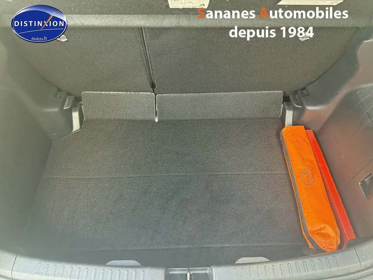 Coffre ouvert de Toyota Yaris Hybrid 116h 2023 en peinture INC, montrant un rangement avec trousse de secours orange.