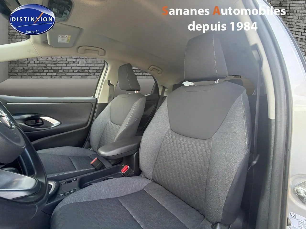 Vue intérieure côté avant droit de la Toyota Yaris Hybrid 2023 avec sellerie tissu gris et accoudoir central.
