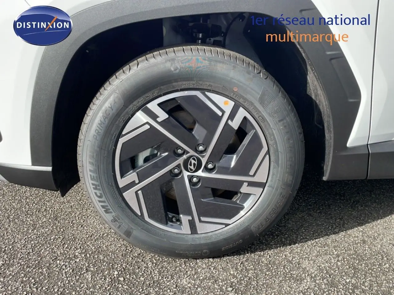 Gros plan sur la roue avant gauche du Hyundai Tucson blanc Atlas avec jante alliage noire et grise au design géométrique.