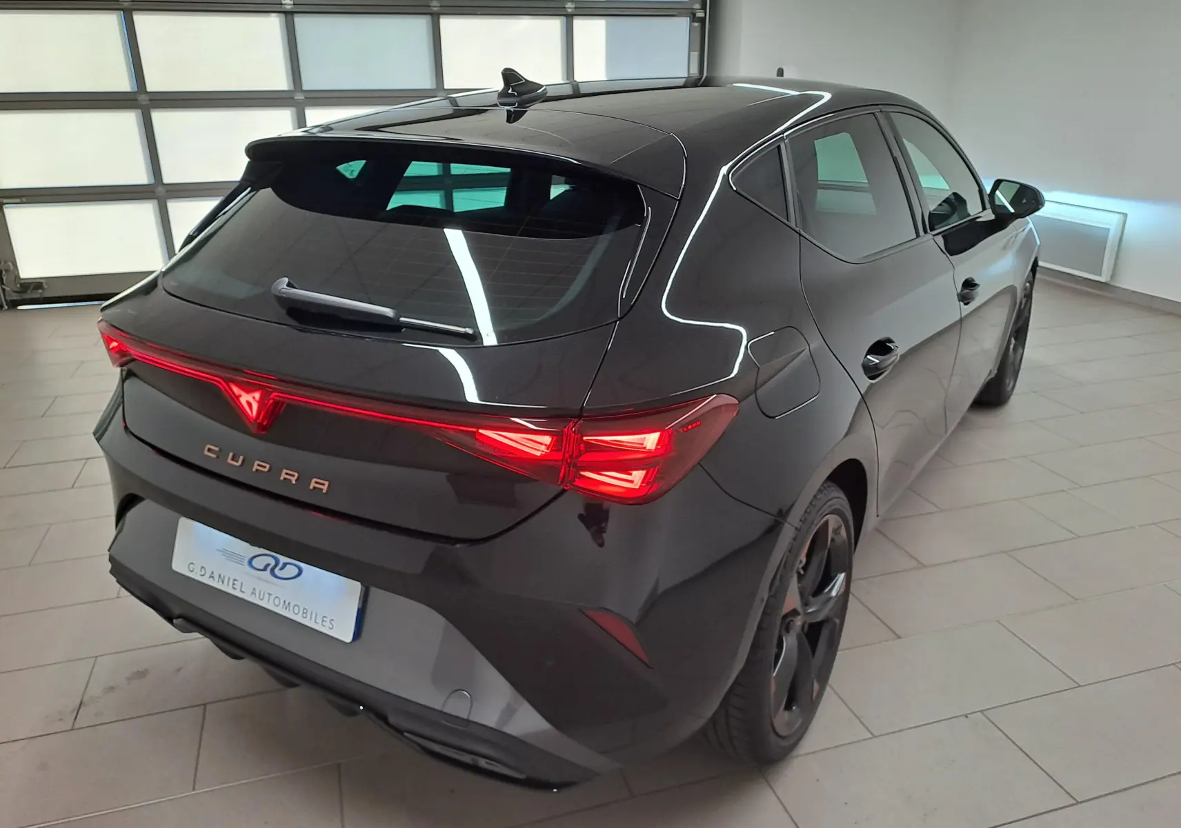 Vue 3/4 arrière droite d'une CUPRA Leon 2025 Noir Minuit avec feux arrière allumés et jantes cuivrées 18 pouces.