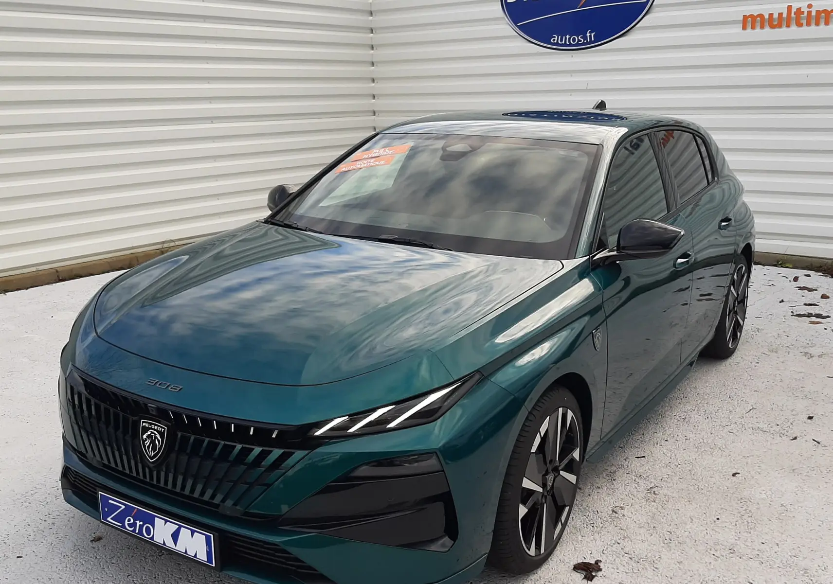 Vue 3/4 avant d'une Peugeot 308 2026 bleu Lagoa avec calandre noire et phares LED fins, stationnée devant un mur blanc.