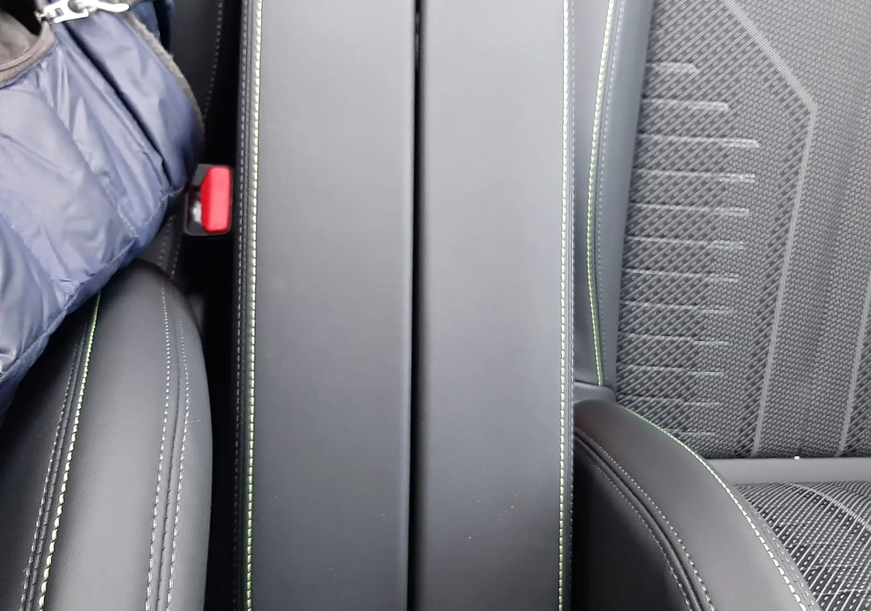 Vue rapprochée de l'accoudoir central noir avec surpiqûres vertes entre les sièges avant en tissu et cuir gris d'une Peugeot 308.