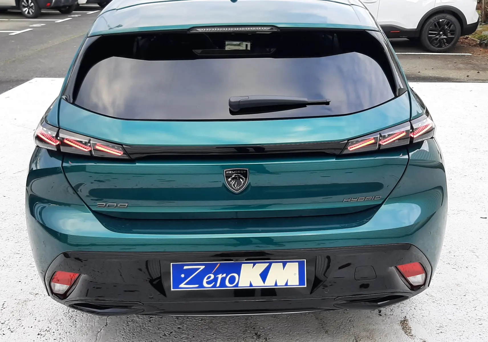 Vue arrière d'une Peugeot 308 hybride bleu Lagoa avec feux LED distinctifs et plaque Zéro KM.