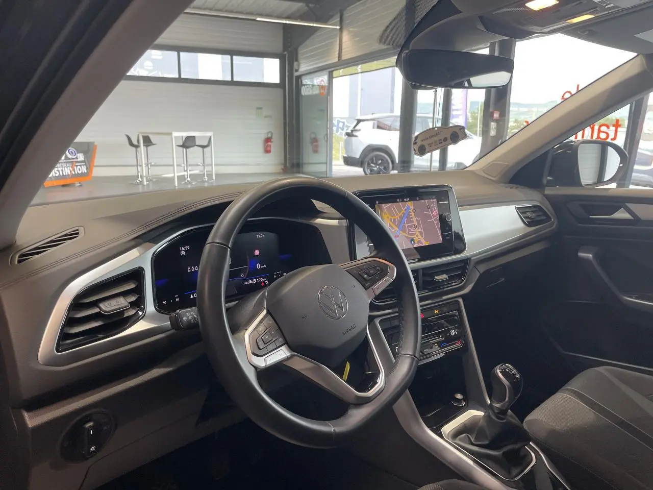 Vue intérieure côté conducteur du Volkswagen T-Roc 2025 gris Indium, avec volant cuir multifonction et écran tactile central.