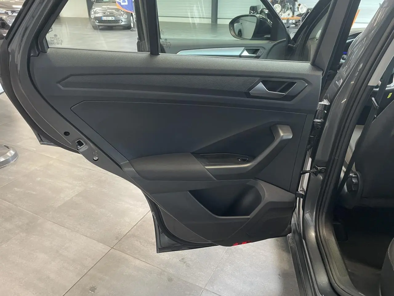 Vue intérieure de la porte arrière gauche du Volkswagen T-Roc Indium Gray 2025 avec garniture noire et poignée argentée.