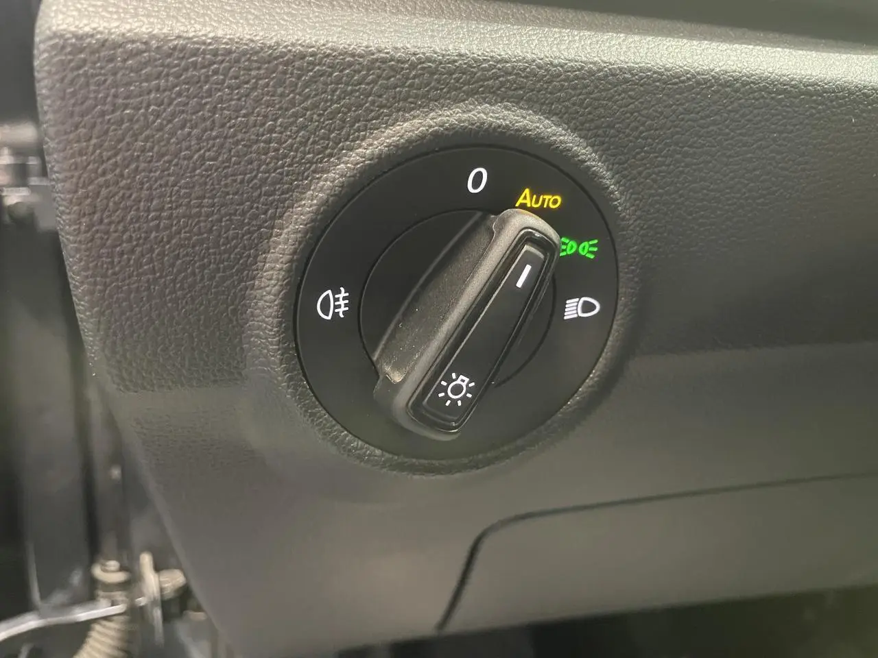 Gros plan sur le bouton de commande des phares du Volkswagen T-Roc, tableau de bord noir texturé.