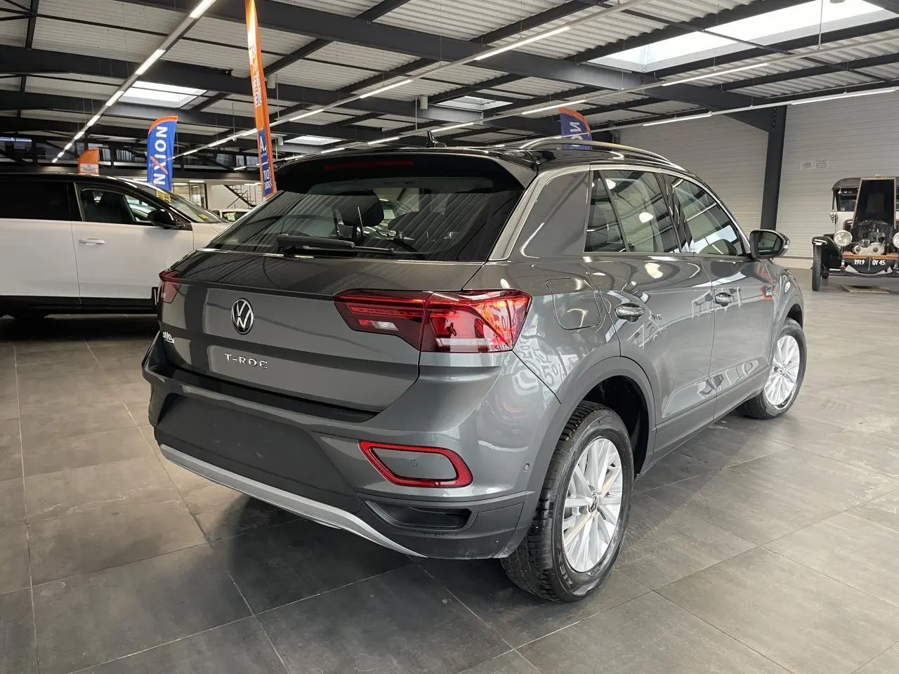 Vue 3/4 arrière droite du Volkswagen T-Roc gris Indium métallisé avec toit noir en intérieur d'exposition.