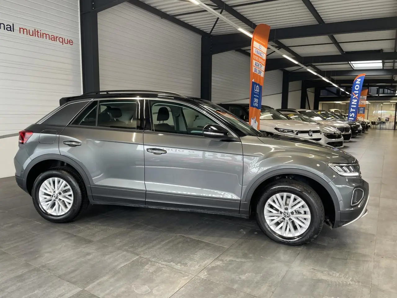 Volkswagen T-Roc 2025 gris Indium, vue de profil côté gauche en intérieur avec toit noir et jantes alliage.
