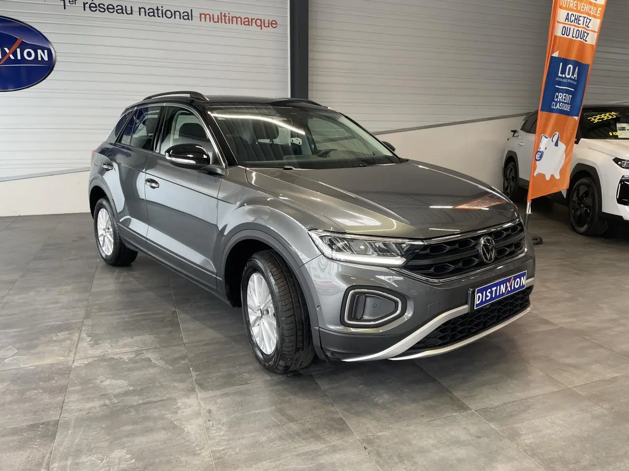 Volkswagen T-Roc gris Indium en 3/4 avant droit, avec toit noir et jantes alliage 16 pouces en showroom.