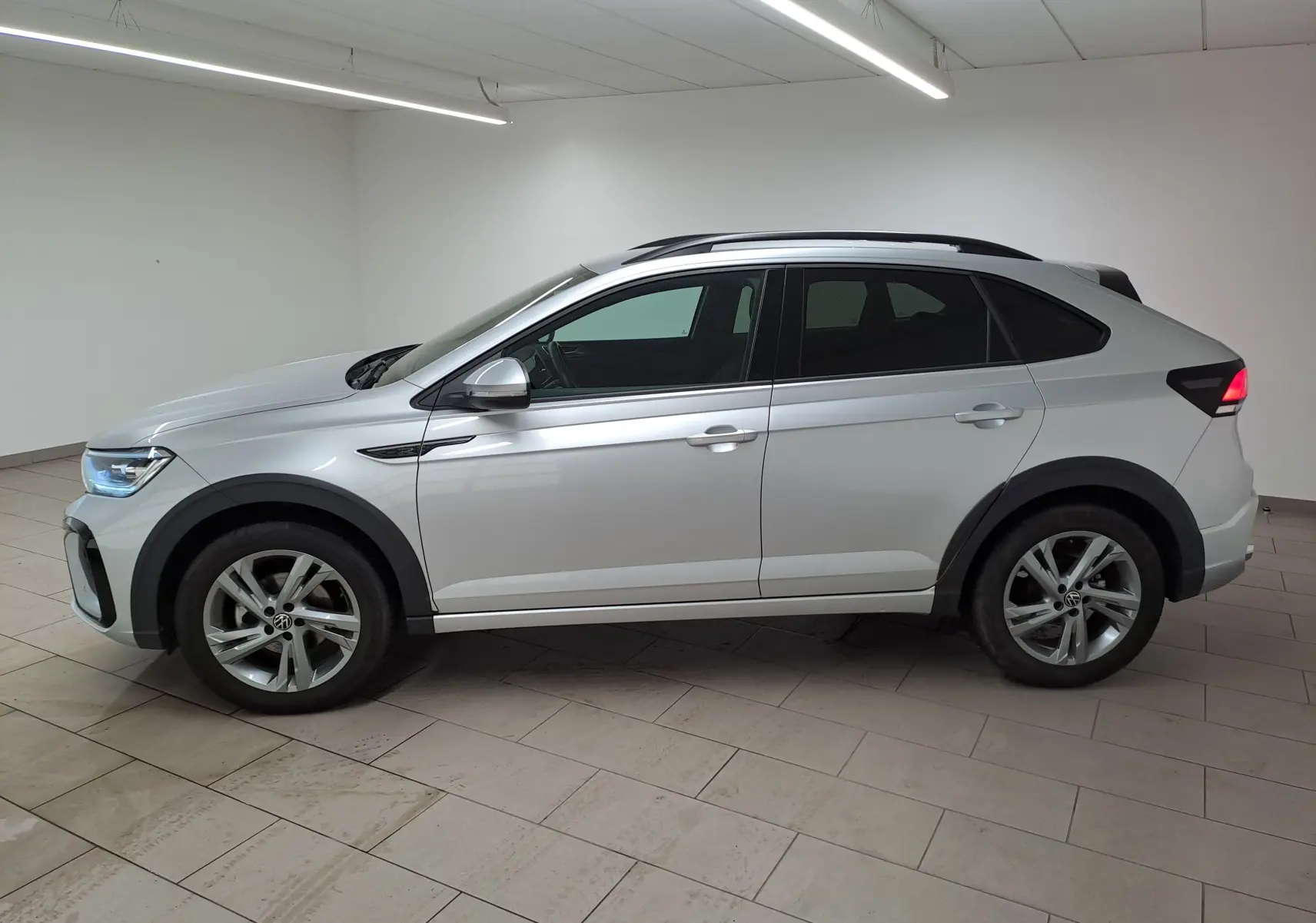 Volkswagen Taigo R-Line 2024 en reflet d'argent, vue profil côté gauche avec jantes alliage et feux arrière allumés.