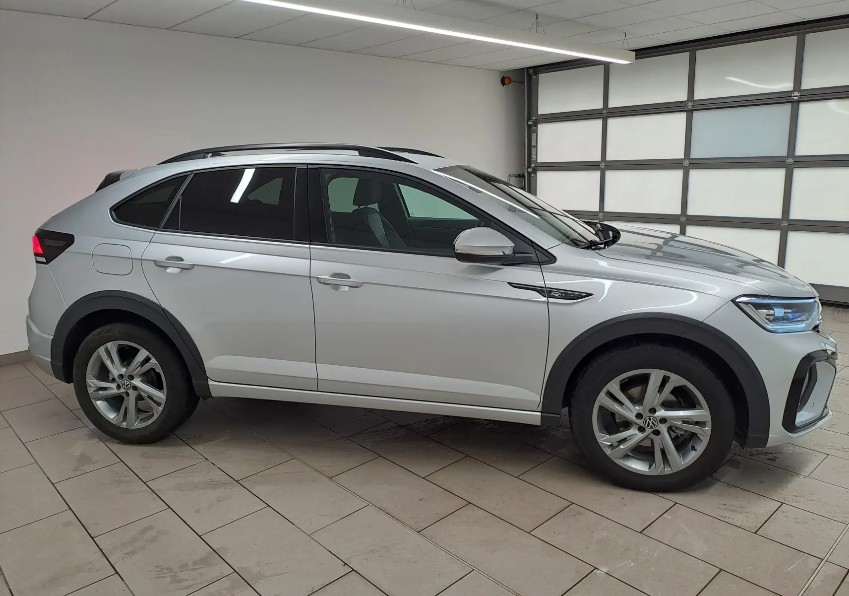 Volkswagen Taigo 2024 R-Line en peinture métallisée reflet d'argent, vue profil côté gauche dans un garage lumineux.