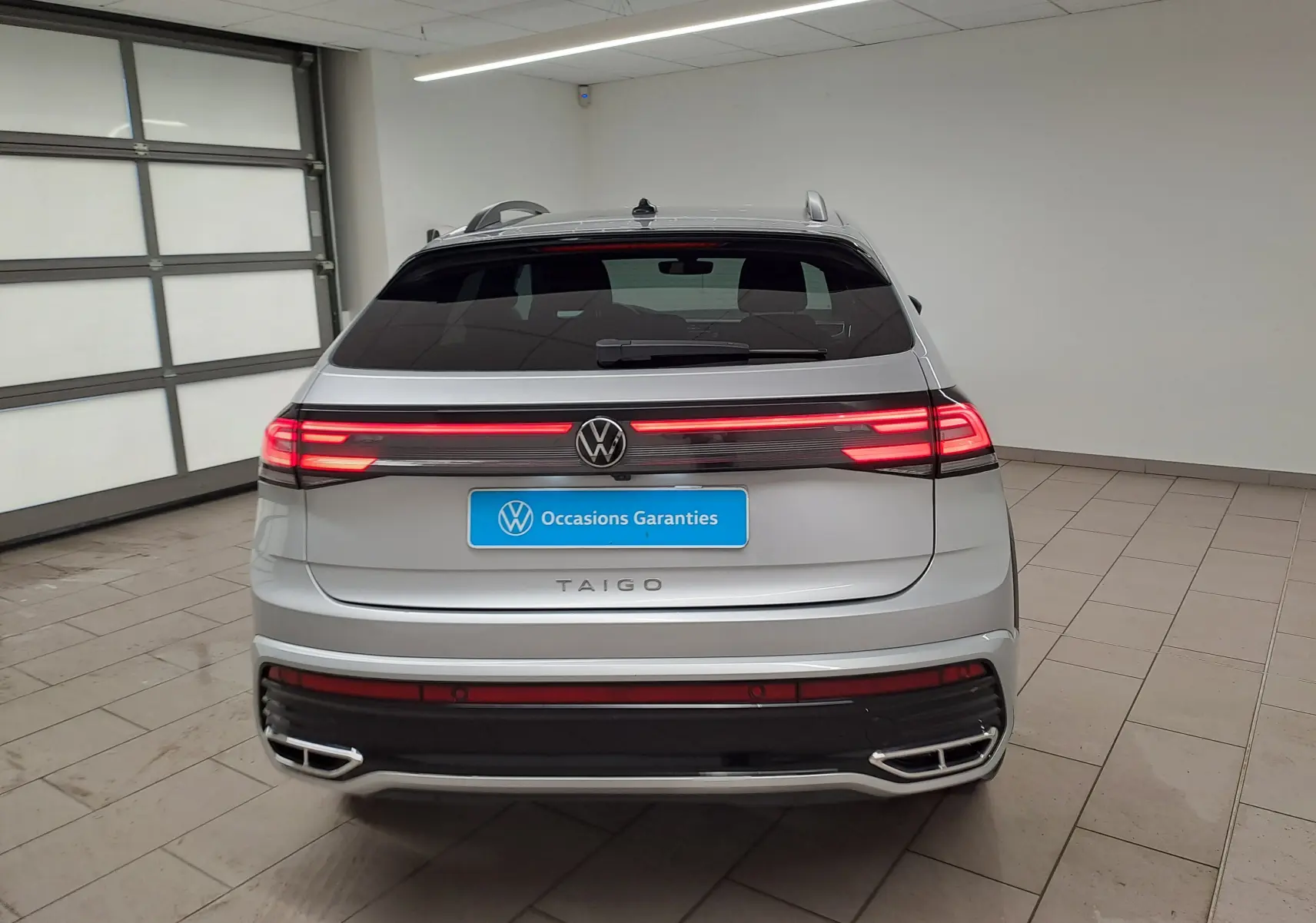 Vue arrière du Volkswagen Taigo 1.0 TSI 110 DSG7 R-LINE 2024 en peinture métallisée Reflet d'argent avec feux LED allumés.