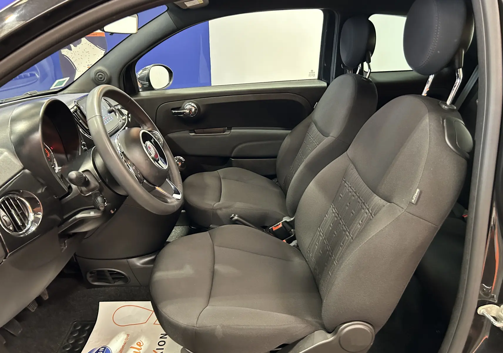 Vue intérieure côté gauche de la Fiat 500 noire 2023, montrant les sièges en tissu et le tableau de bord compact.