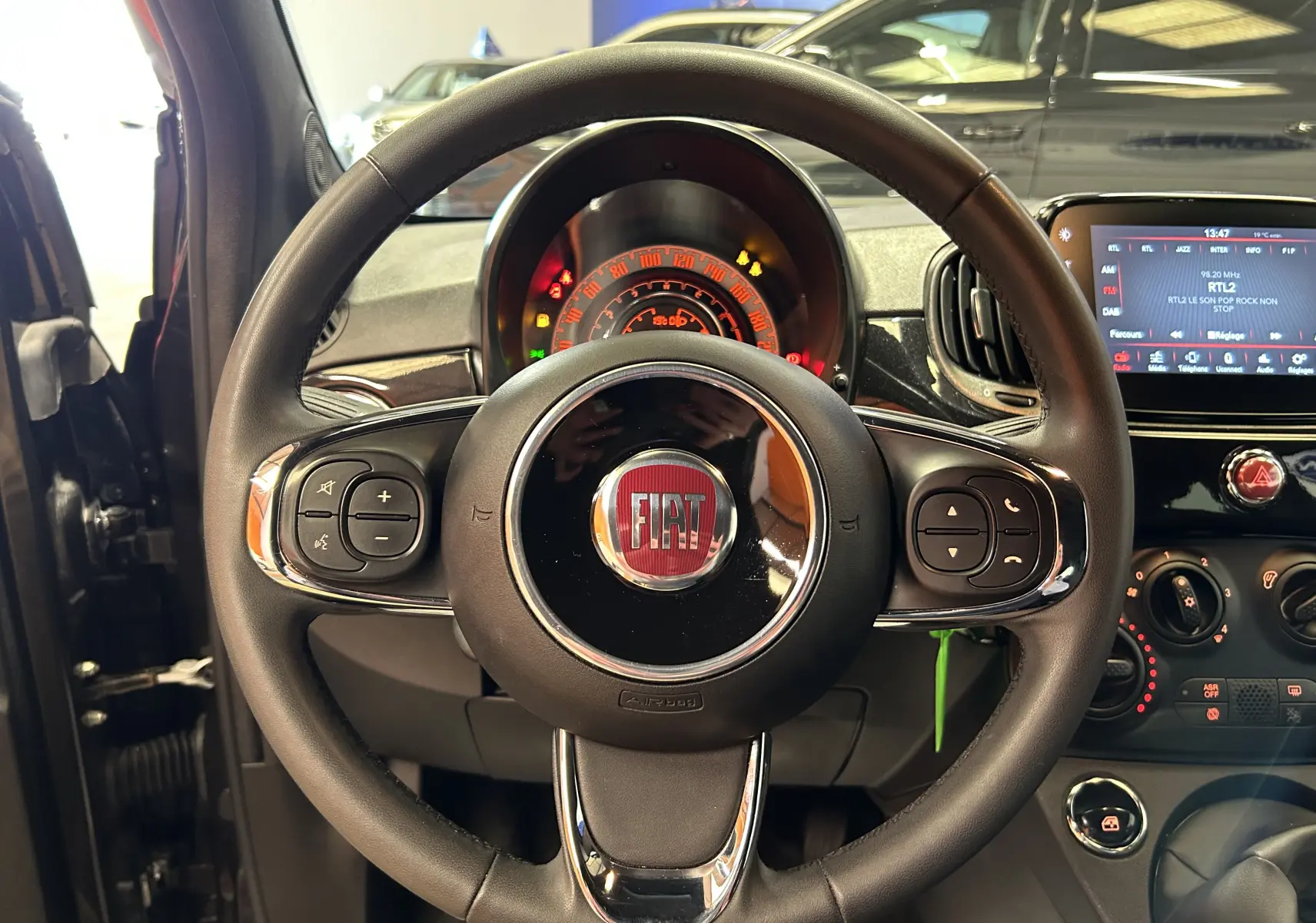 Vue rapprochée du volant noir de la Fiat 500 2023 avec tableau de bord et écran tactile en arrière-plan.
