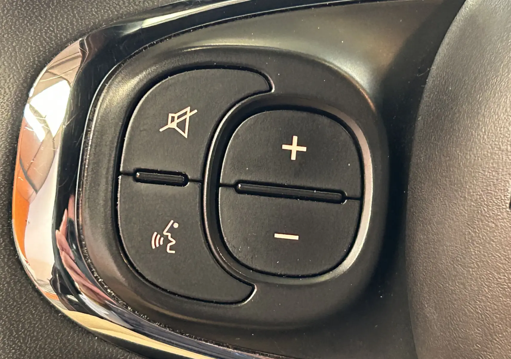 Gros plan sur les commandes de volume et de coupure du son au volant d'une Fiat 500 noire de 2023.