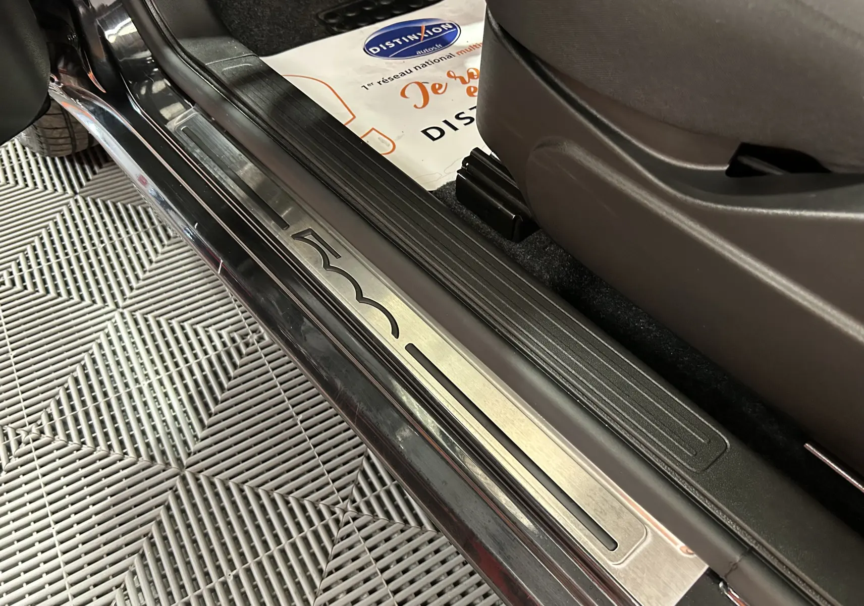 Gros plan sur la plaque de seuil de porte noire de la FIAT 500 2023 avec logo gravé et intérieur tissu sombre.