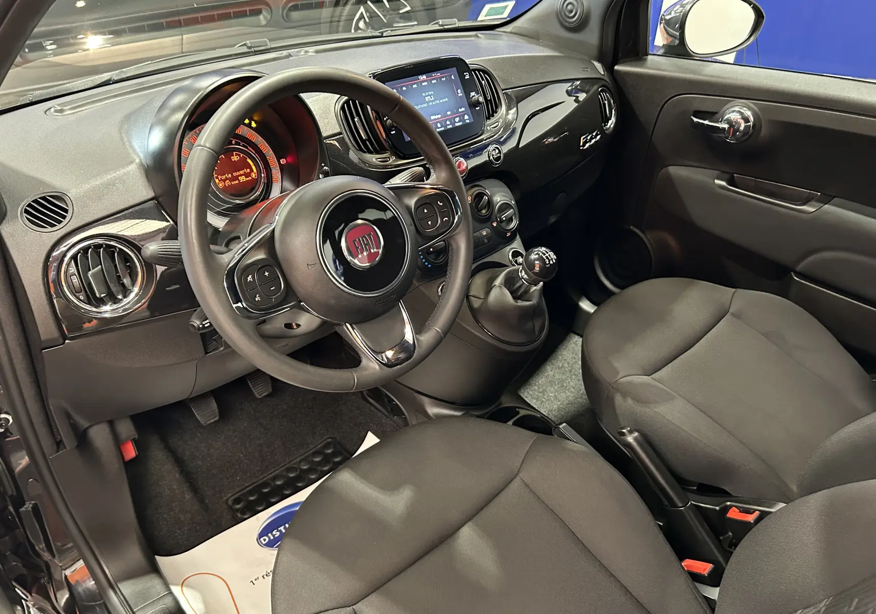 Intérieur de la Fiat 500 noir vue côté conducteur, tableau de bord avec écran tactile et volant multifonction.