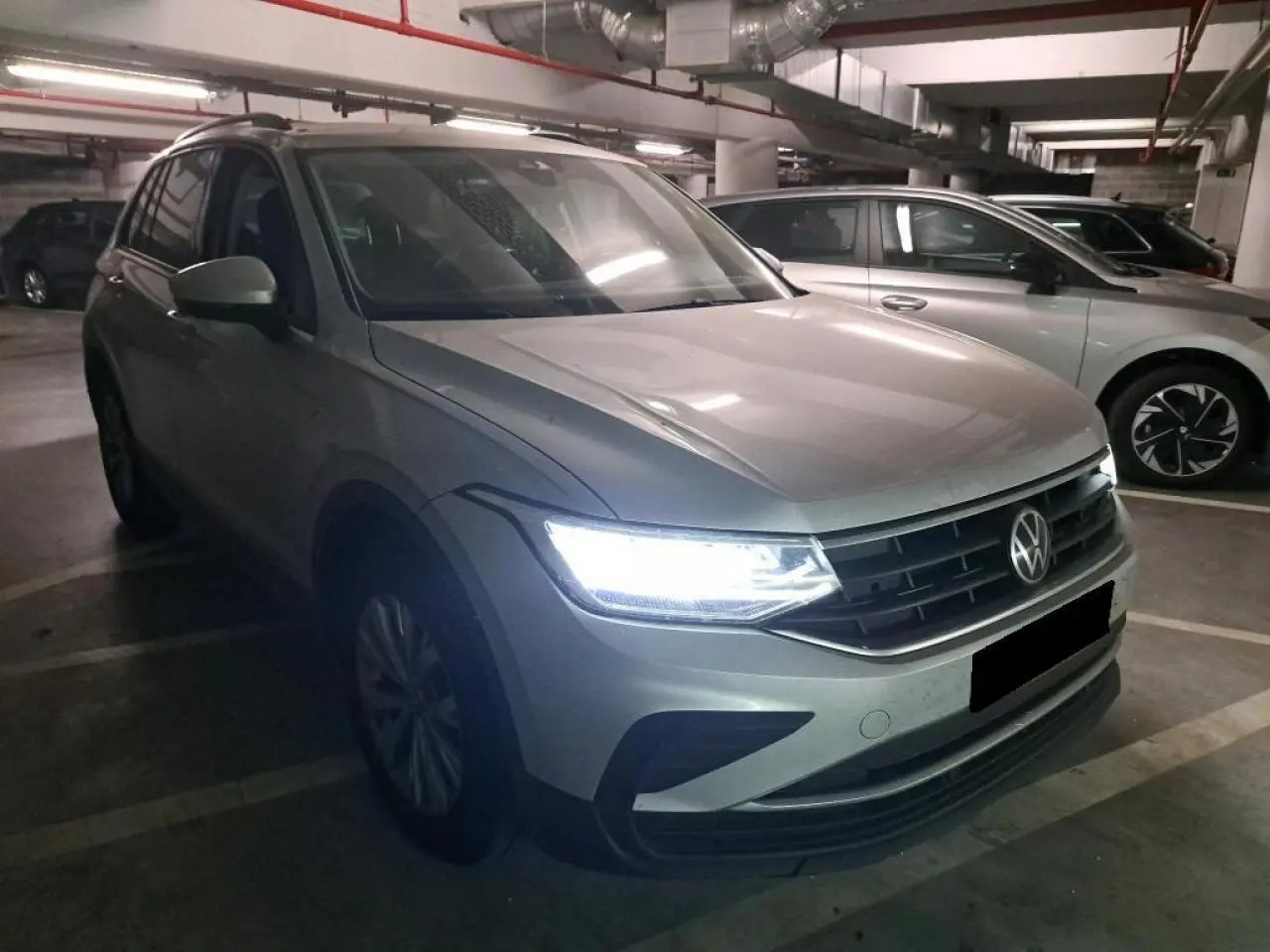 Volkswagen Tiguan 2.0 TDI 2022 en argent fleuret, vue 3/4 avant avec phares LED allumés dans un parking.