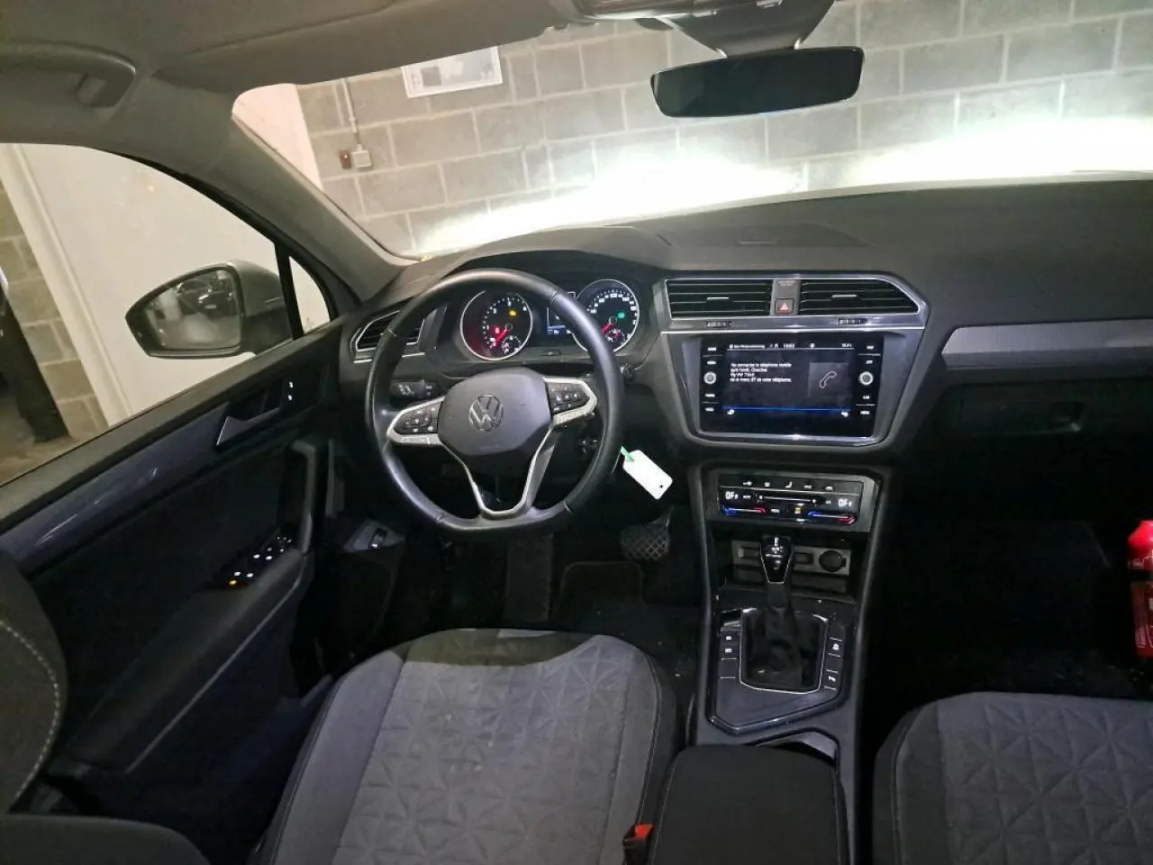 Vue intérieure du Volkswagen Tiguan 2022, tableau de bord et volant multifonctions en cuir, ambiance sombre et moderne.