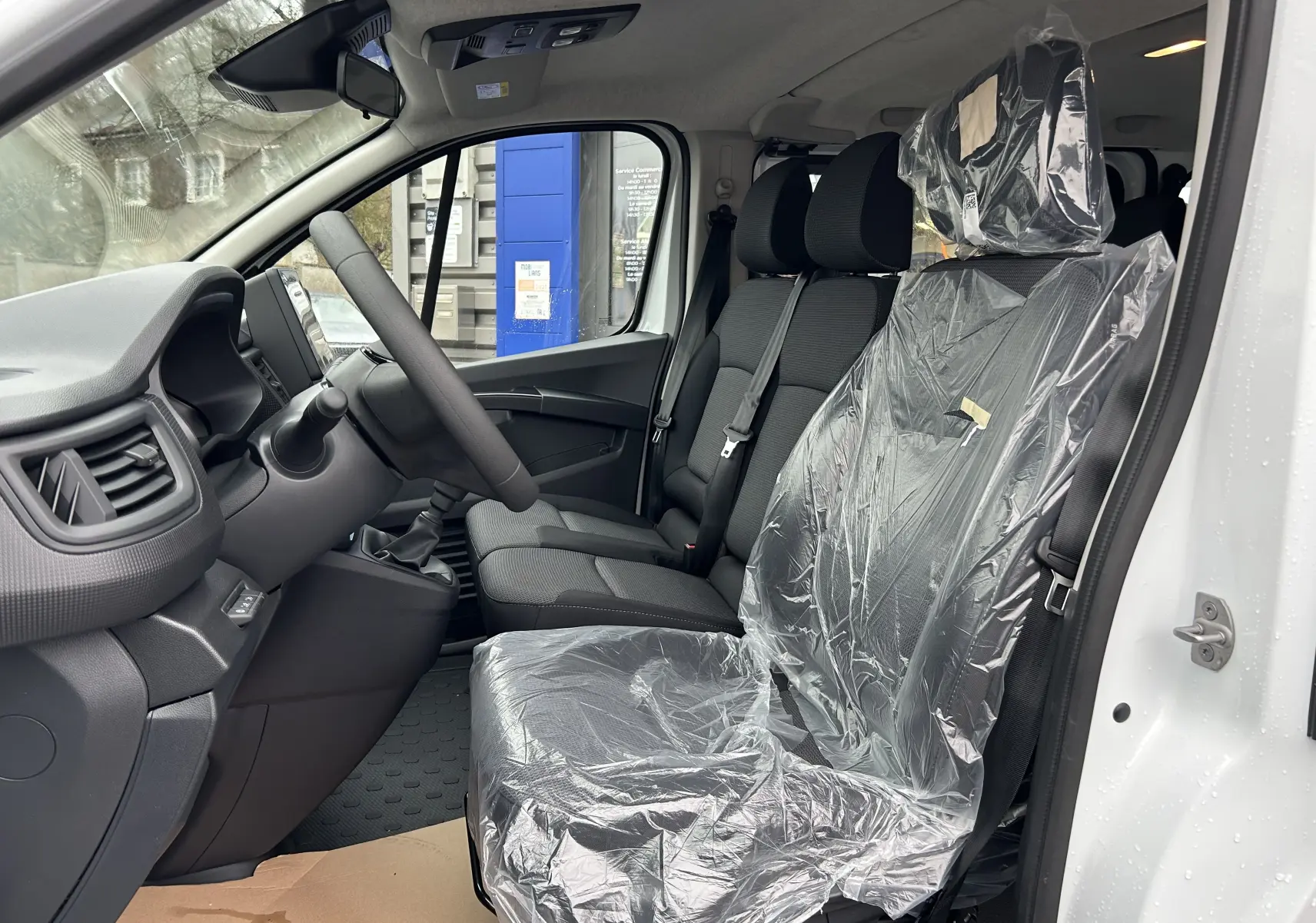 Vue intérieure côté conducteur du Renault Trafic Combi blanc glacier 2025, sièges avant en tissu protégés par housses plastiques.