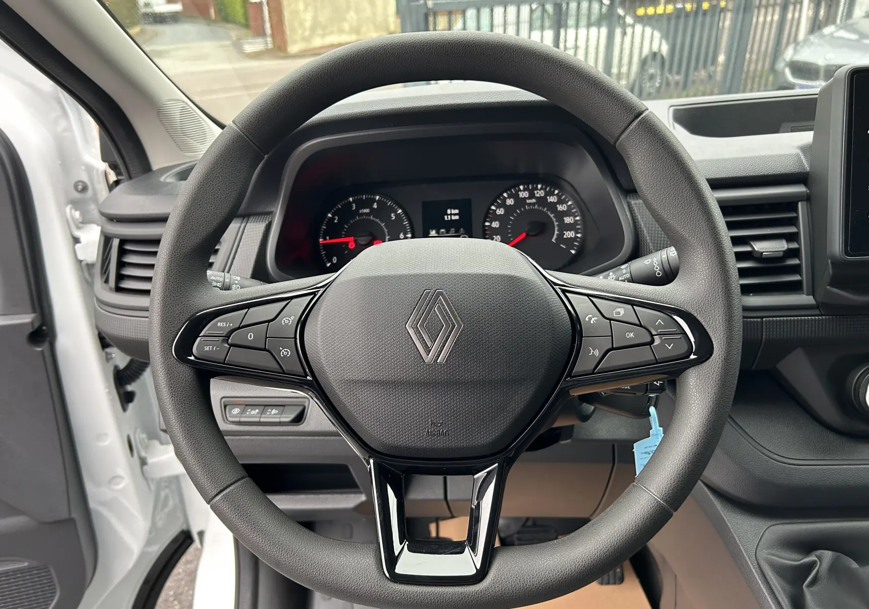Vue centrée sur le volant noir du Renault Trafic Combi blanc glacier, avec tableau de bord et portière ouverte côté gauche visible.