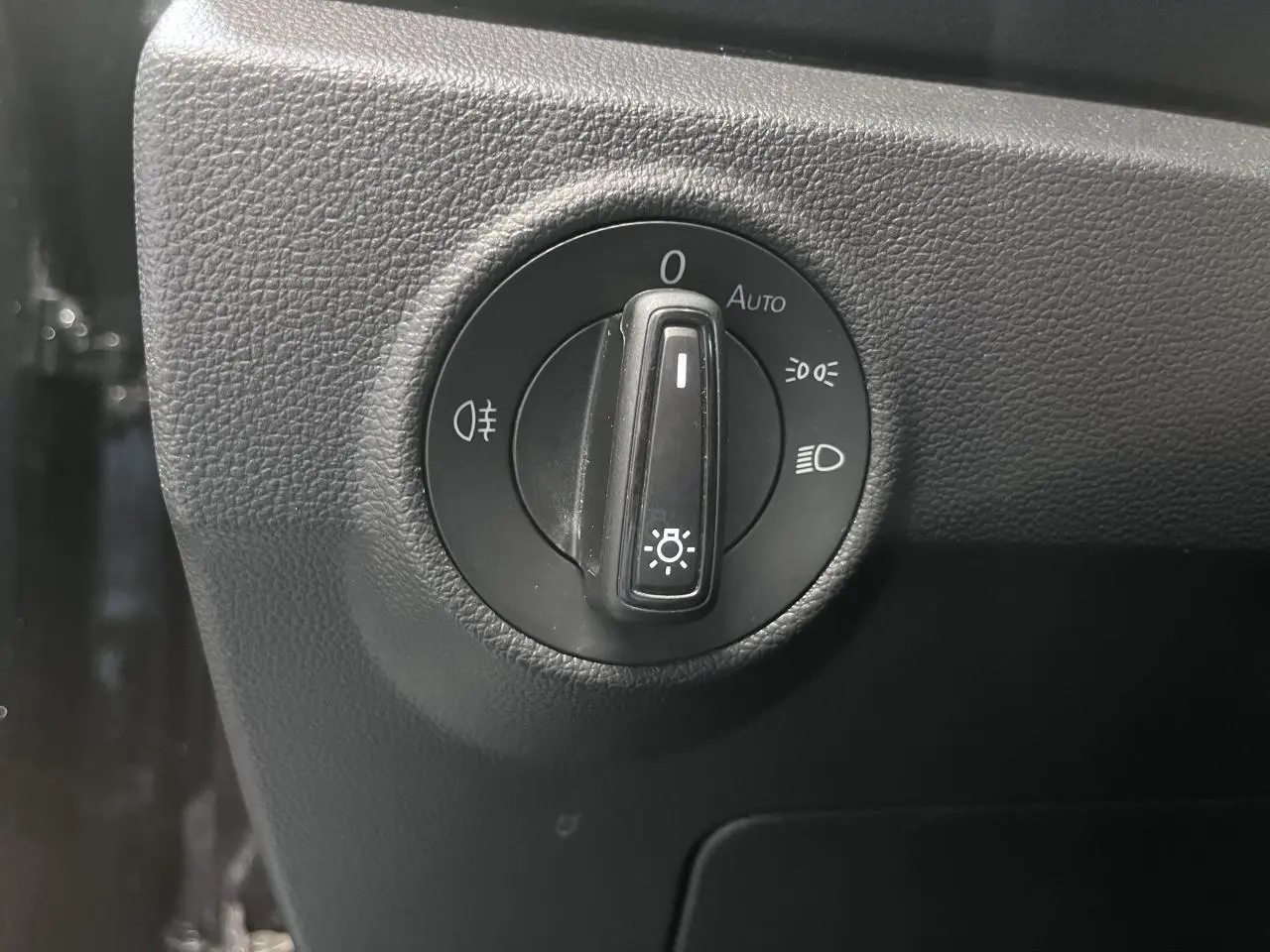 Gros plan sur le bouton de commande des phares dans l’habitacle noir du Volkswagen T-Roc Deep Black Pearlescent.