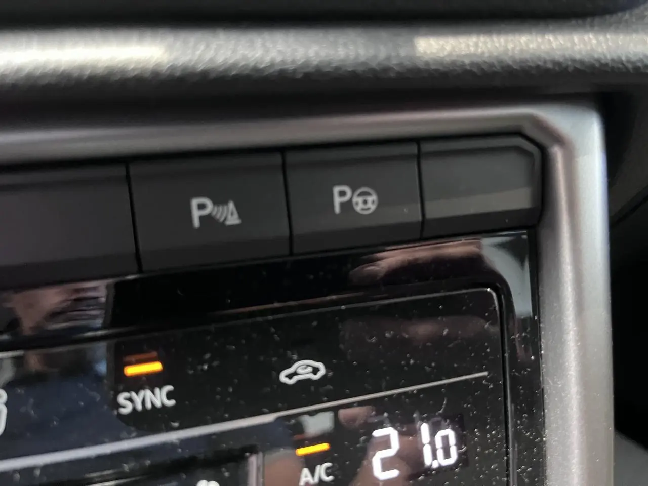 Gros plan sur la console centrale du Volkswagen T-Roc 2025, affichant la climatisation à 21°C en mode sync.