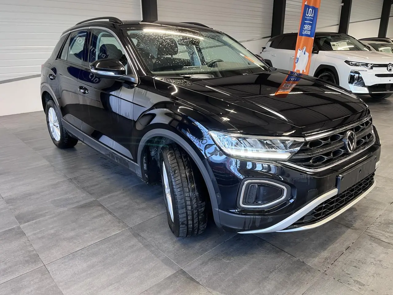 Volkswagen T-Roc Deep Black Pearlescent vue 3/4 avant droit en intérieur avec phares LED allumés.