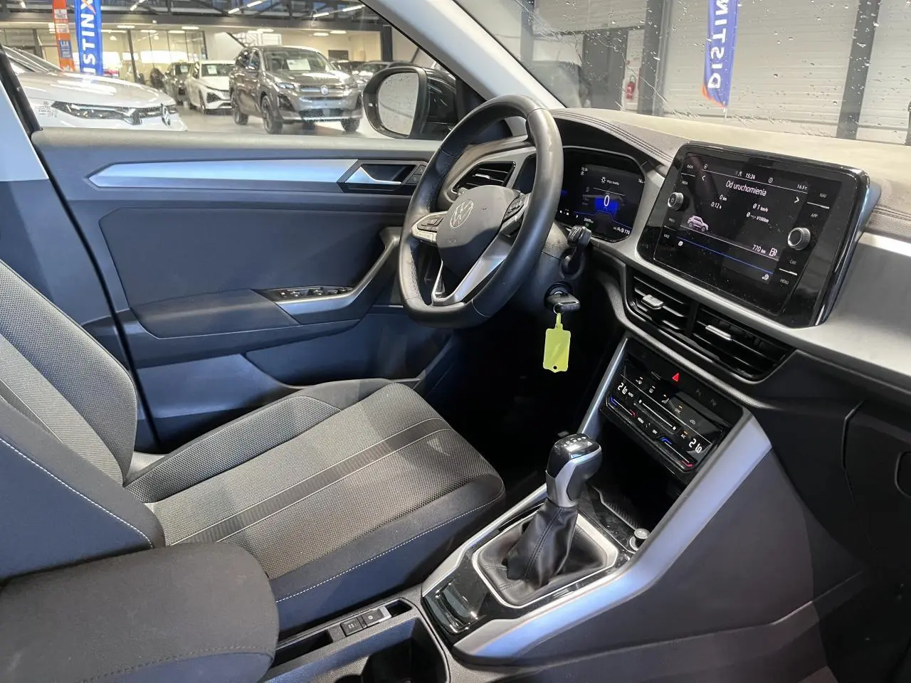 Intérieur avant droit du Volkswagen T-Roc 2025 avec sellerie tissu noire et tableau de bord digital.
