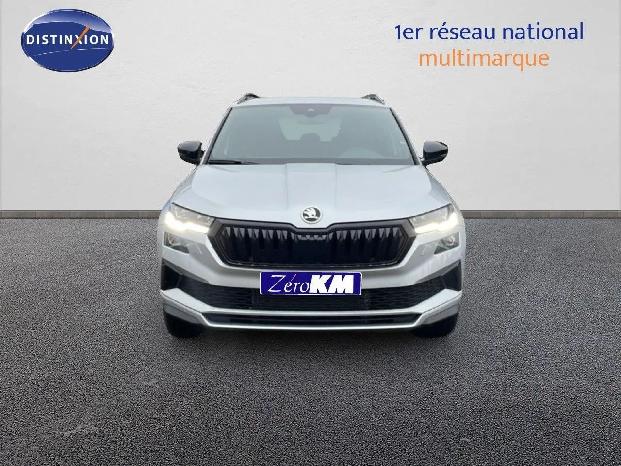 Vue avant d’un Skoda Karoq gris argent métallisé avec calandre noire et phares allumés sur fond neutre.