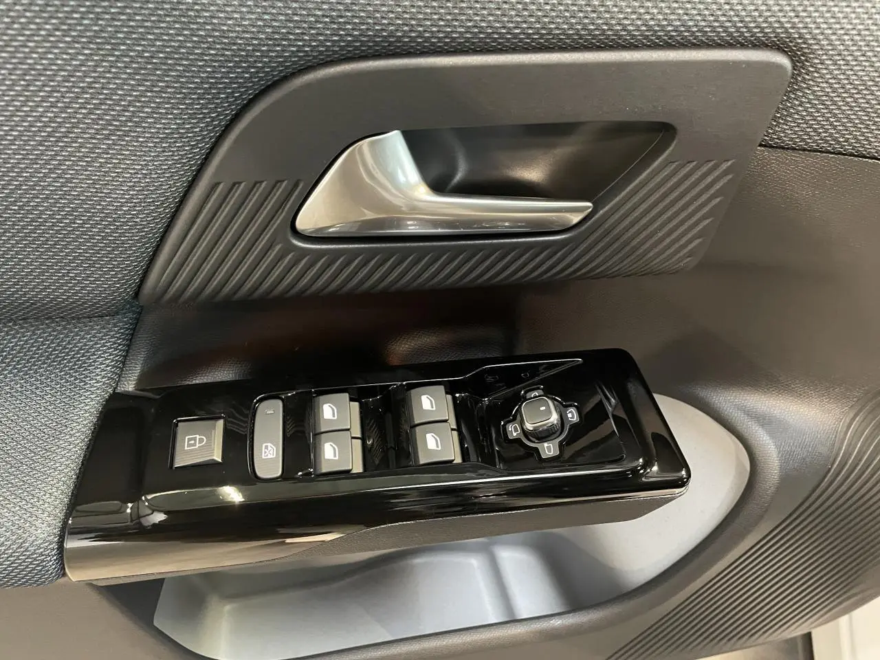 Gros plan sur la commande de lève-vitres et rétroviseurs côté conducteur du Citroën C5 Aircross 2026 avec garniture noire texturée.