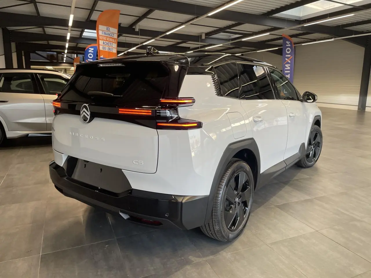 Vue 3/4 arrière droite du Citroën C5 Aircross blanc Okenite avec toit noir et feux arrière LED allumés en intérieur showroom.