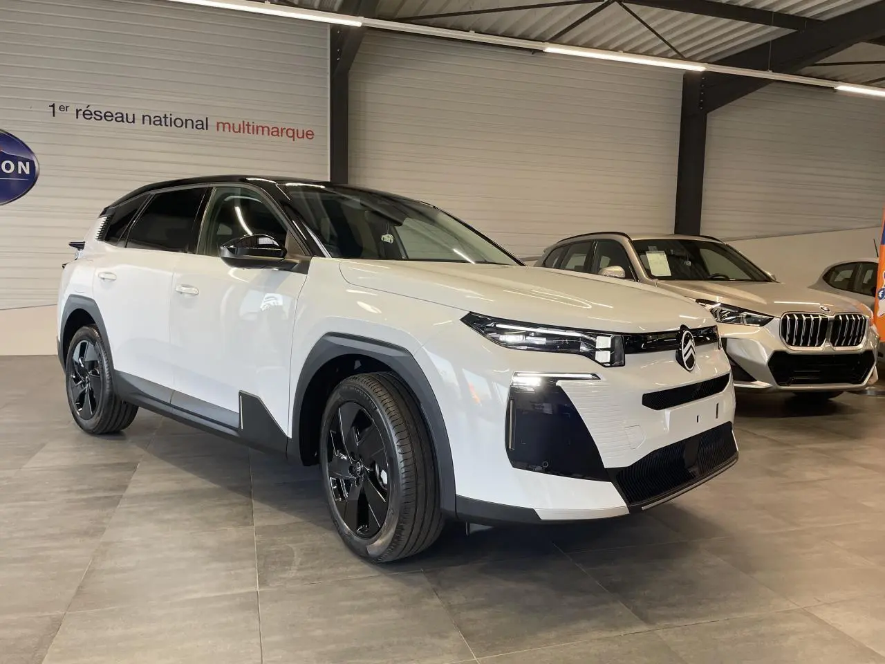 Vue 3/4 avant d'un Citroën C5 Aircross blanc Okenite avec toit noir et jantes alliage noires en showroom.