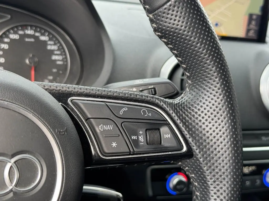 Gros plan sur le volant en cuir perforé de l'Audi A3 Cabriolet gris, avec commandes multimédia et tableau de bord flou en arrière-plan.