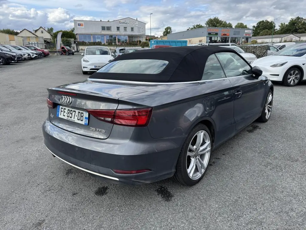 Audi A3 Cabriolet gris vue 3/4 arrière droit avec capote noire en position fermée sur parking extérieur.