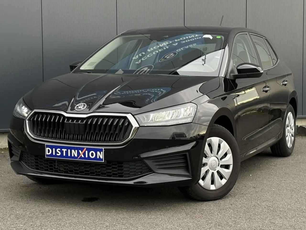 Vue 3/4 avant d'une Skoda Fabia 2024 noir Magic garée sur un sol pavé devant un bâtiment blanc.