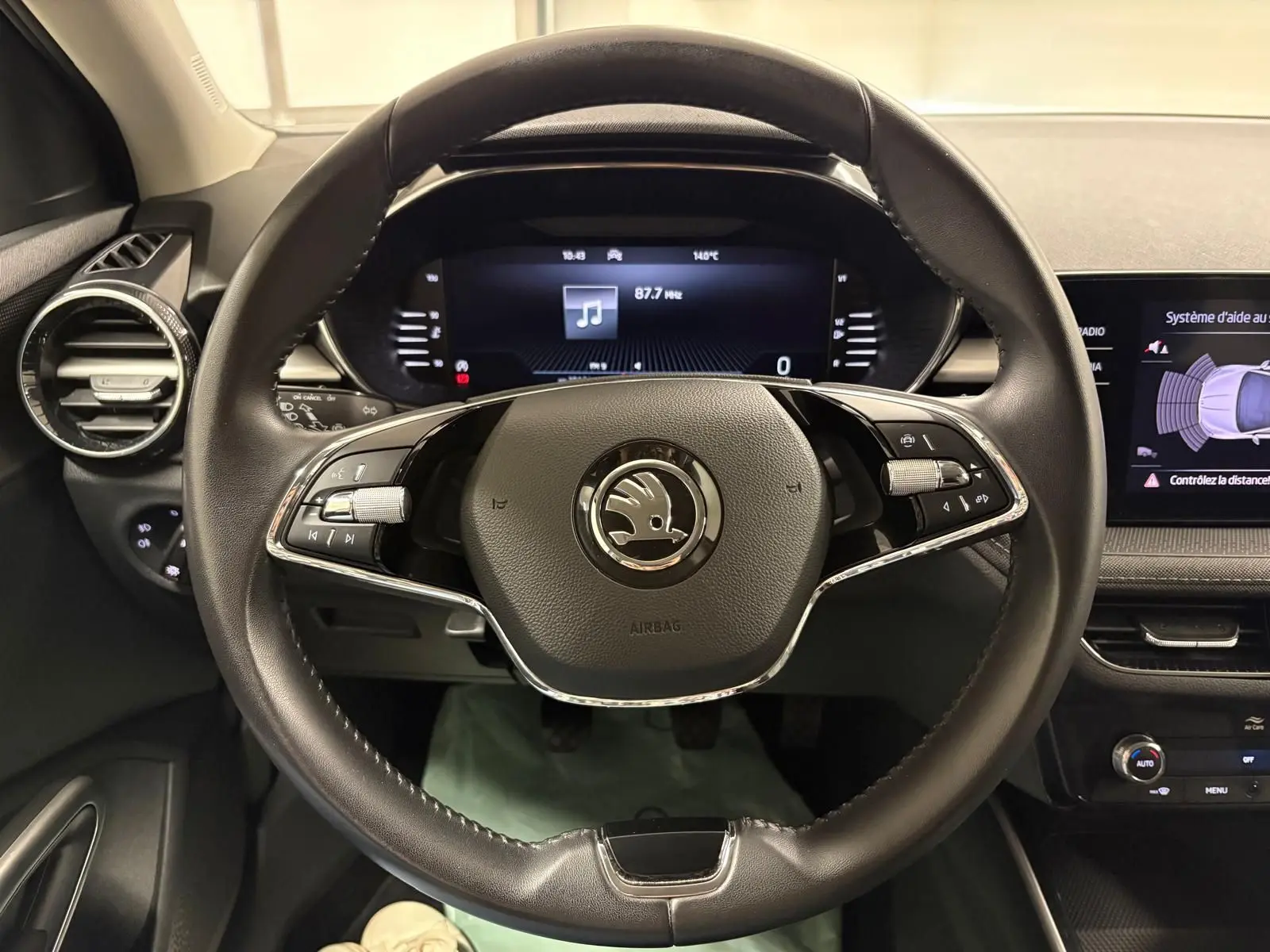 Vue intérieure centrée sur le volant cuir noir de la Skoda Fabia 2023 avec tableau de bord digital et écran d’aide au stationnement.